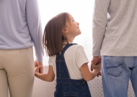 A young girl holding hands with two adults, looking up and smiling at one of them—capturing a moment of warmth and trust, just the kind of bond a Houston family law attorney helps families protect.
