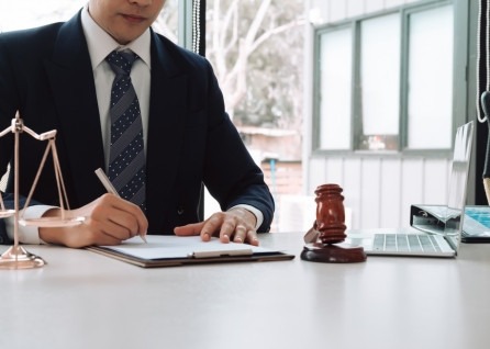 A houston family law attorney in a suit writes on a clipboard at a desk with a gavel, scales of justice, and a laptop.