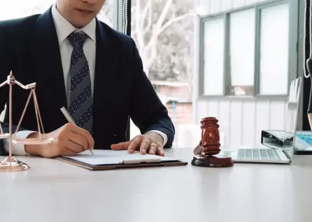 A houston family law attorney in a suit writes on a clipboard at a desk with a gavel, scales of justice, and a laptop.