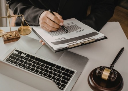 A Houston family law attorney reviews and signs a document on a clipboard next to a laptop, a gavel, and a set of scales of justice on the desk.