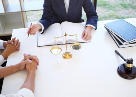 Three people sit at a desk with a scale, legal books, and a gavel, having a discussion with a Houston family law attorney. One person is writing in an open notebook.