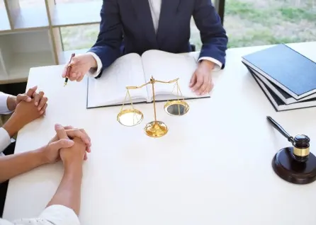 Three people sit at a desk with a scale, legal books, and a gavel, having a discussion with a Houston family law attorney. One person is writing in an open notebook.